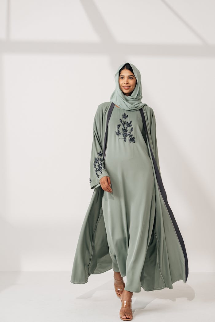 A fashionable adult woman models a sophisticated green abaya indoors, showcasing elegant design.