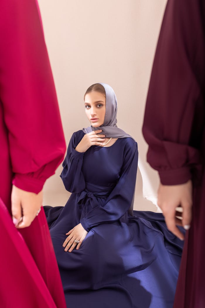 Stylish woman wearing a hijab sitting indoors in a navy abaya, captured in soft light.