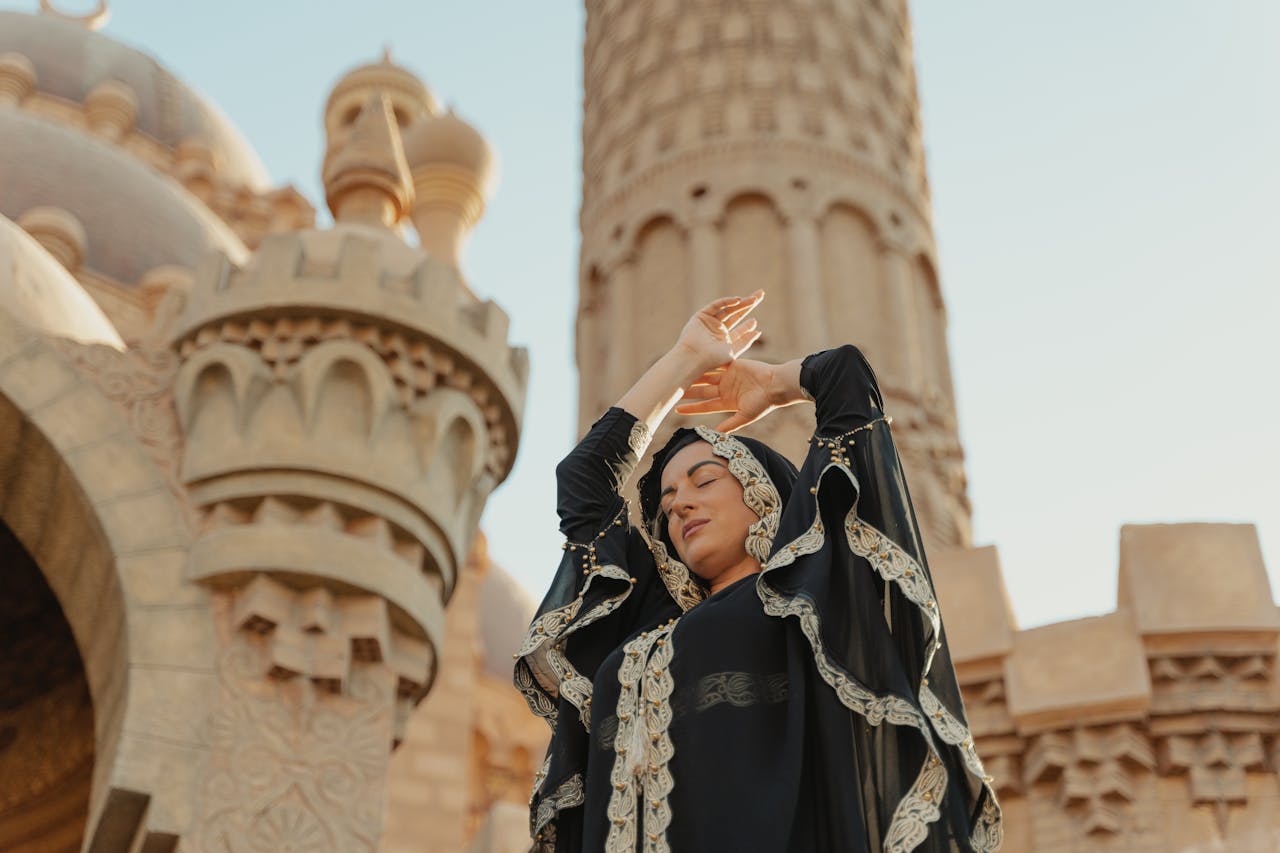 A woman in traditional abaya poses gracefully outside a mosque, embracing spirituality and culture.