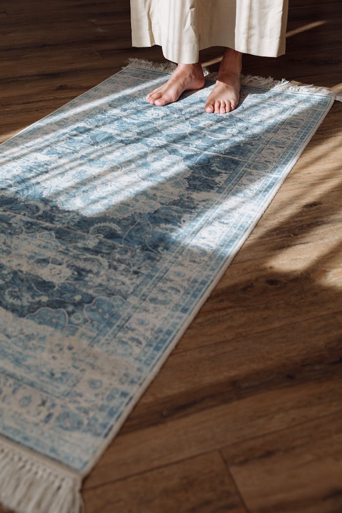 Bare feet on a blue prayer rug with sunlight streaming indoors.