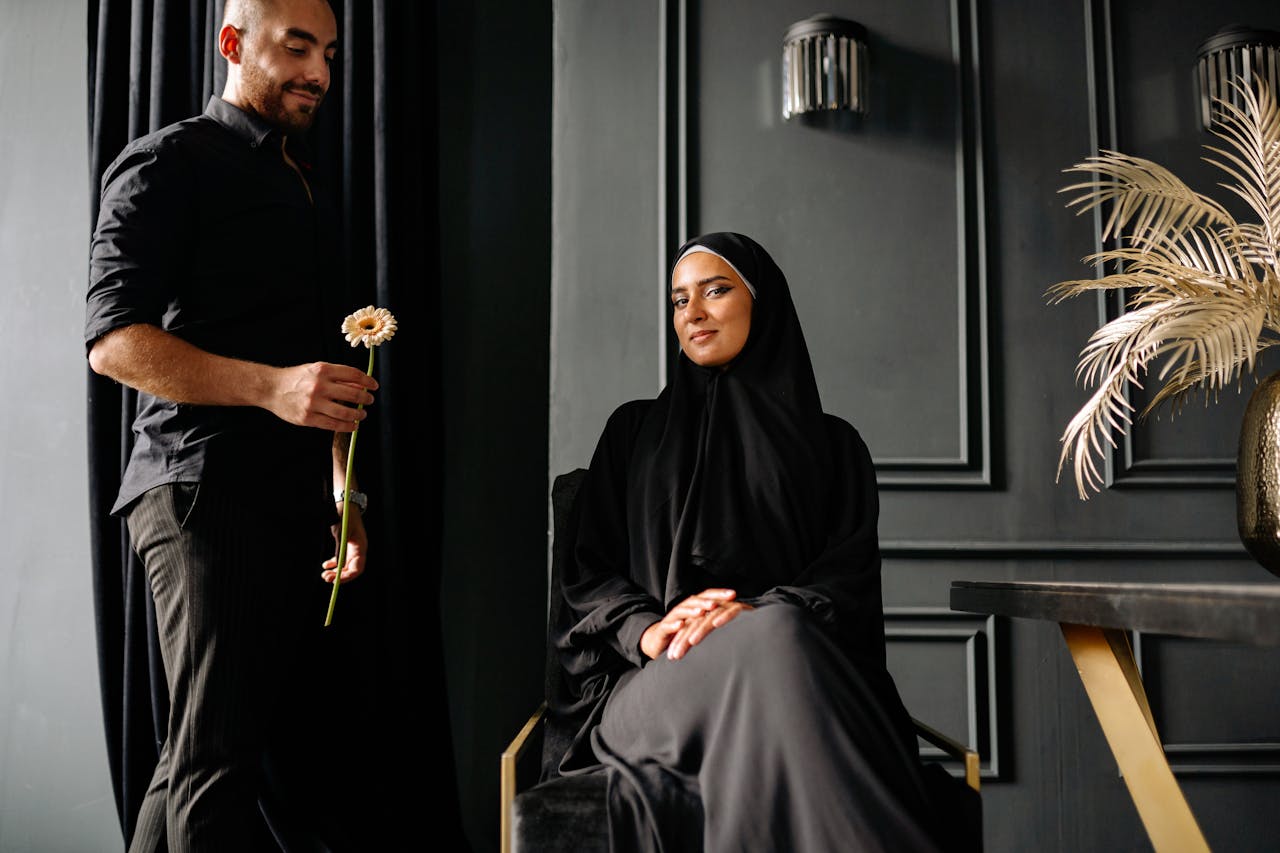 A man offers a flower to a woman in traditional attire indoors, creating a serene and elegant mood.