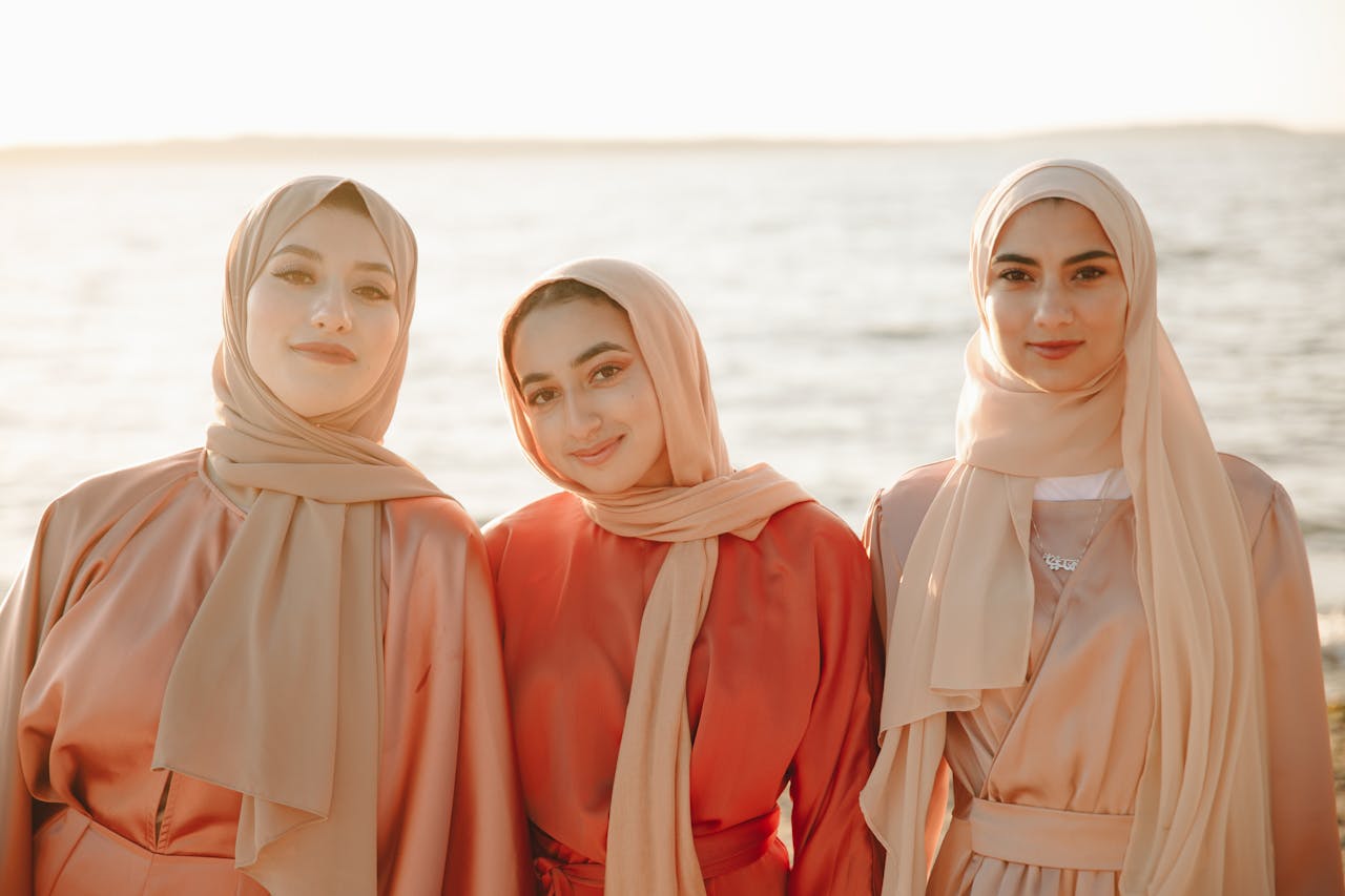 Three smiling women in hijabs enjoying a sunny day at the beach.